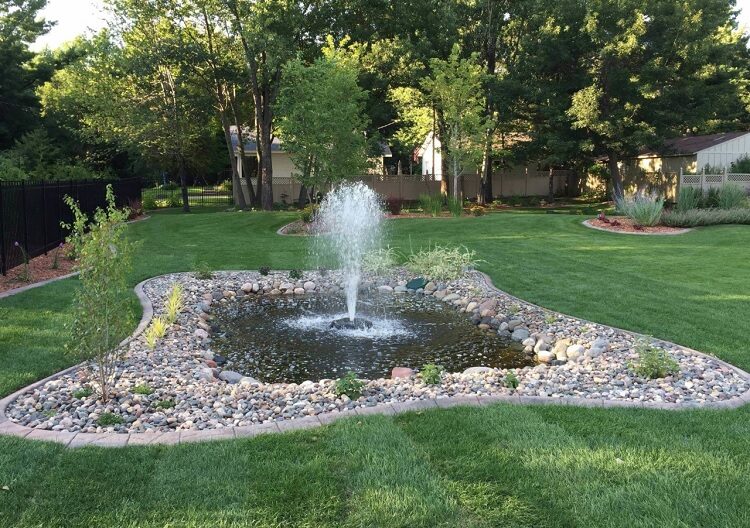 A large fountain that was installed in a homeowner's yard by the Landscape Guys in Minneapolis, MN. It includes rocks, a pond, and a fountain that sprays water in the air.